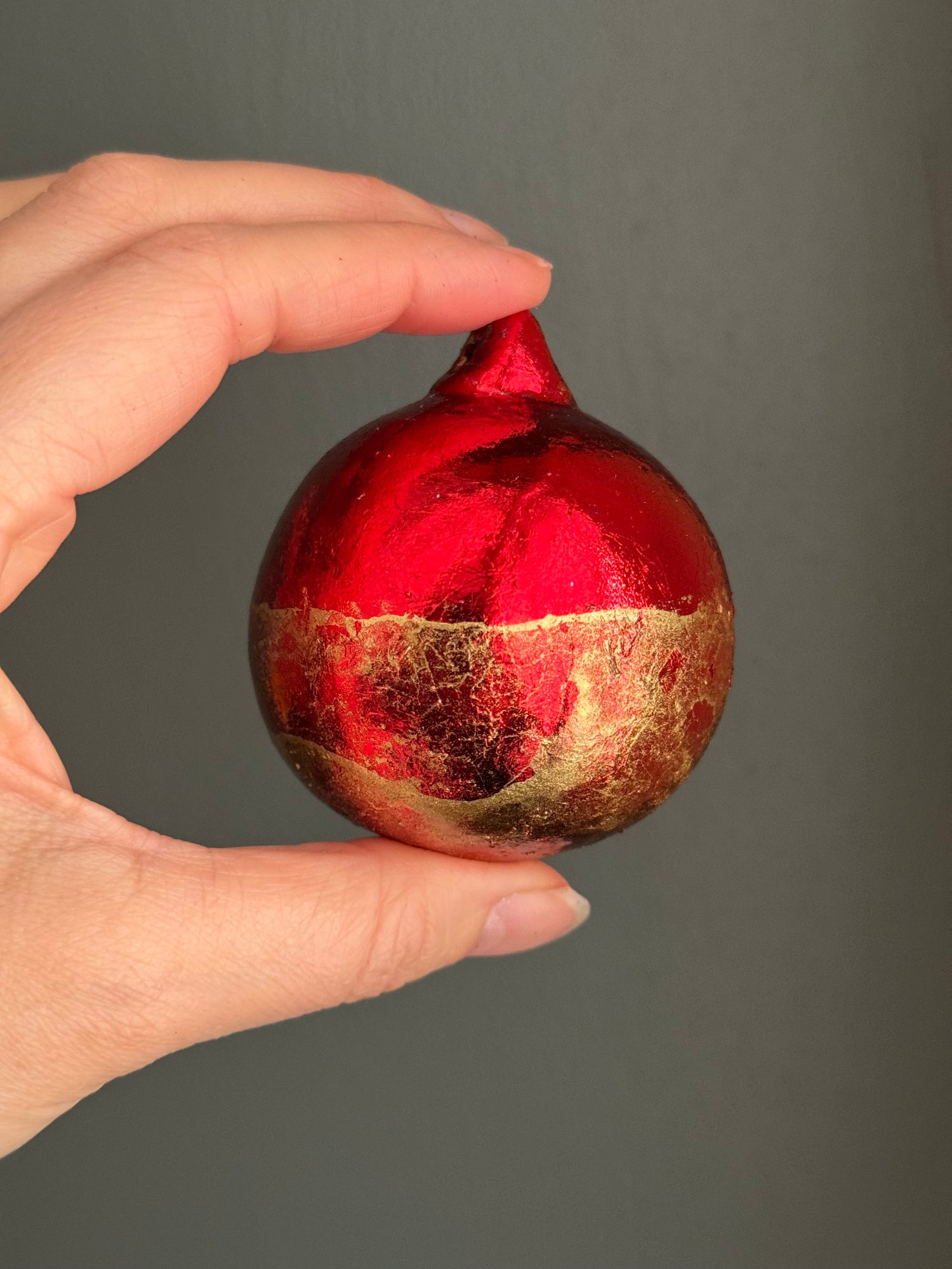 Hand holding a red and gold decorative sphere against a gray background